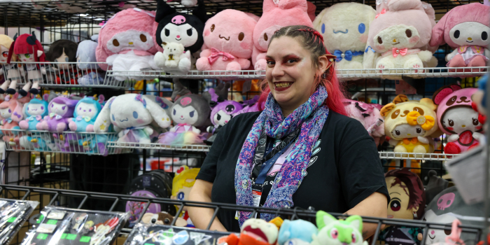 Artist smiles for camera and stands in front of animal plush toys.