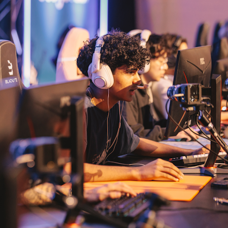 Gamers watch their screens with great focus. They are all wearing white over-ear headsets with microphones to communicate with their team mates. 