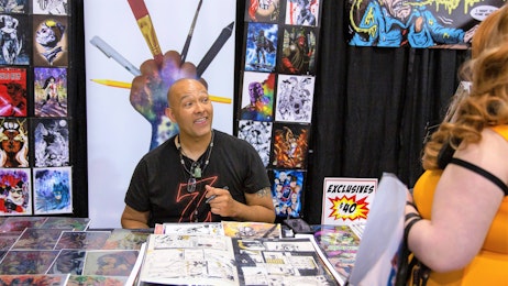 A comic creator is talking to a fan at his table