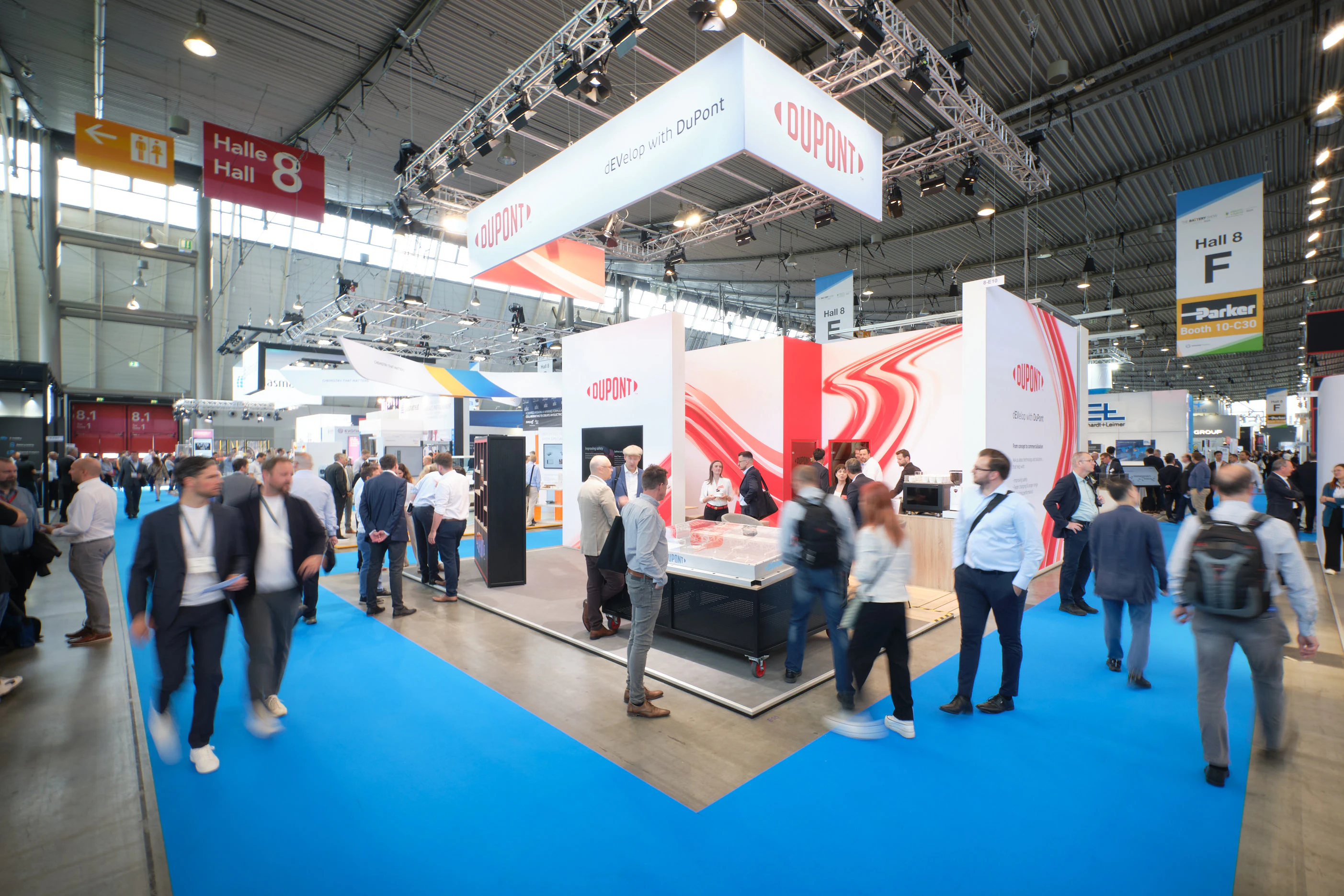 A large crowd of people walking through aisles at a bustling trade show, engaging with various exhibits and displays.