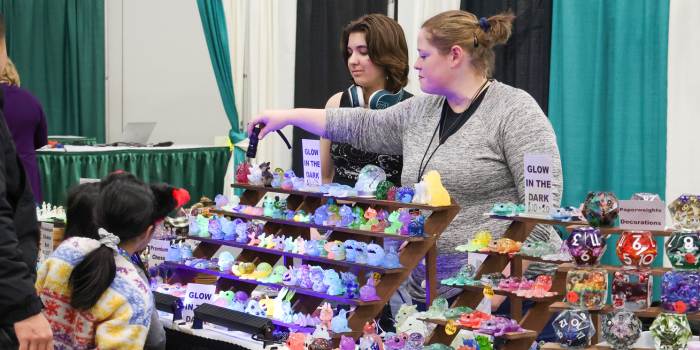 Two artists show off their glowing animal figurine products to two children admiring their event booth.
