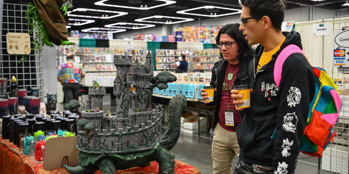 Two customers admire a shopping booth with a large figurine on it depicting a castle on the back of a giant turtle.