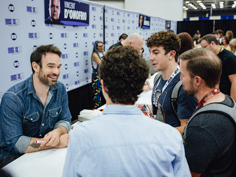 Charlie Cox sitting at his booth, smiling and talking to 3 men in front of him.