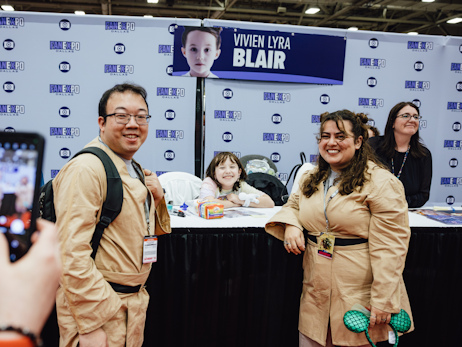 A man (left), Vivien Lyra Blair (middle), and a woman (right) posing together for a photo at Vivien's booth. The man and woman are cosplaying as Jedi.