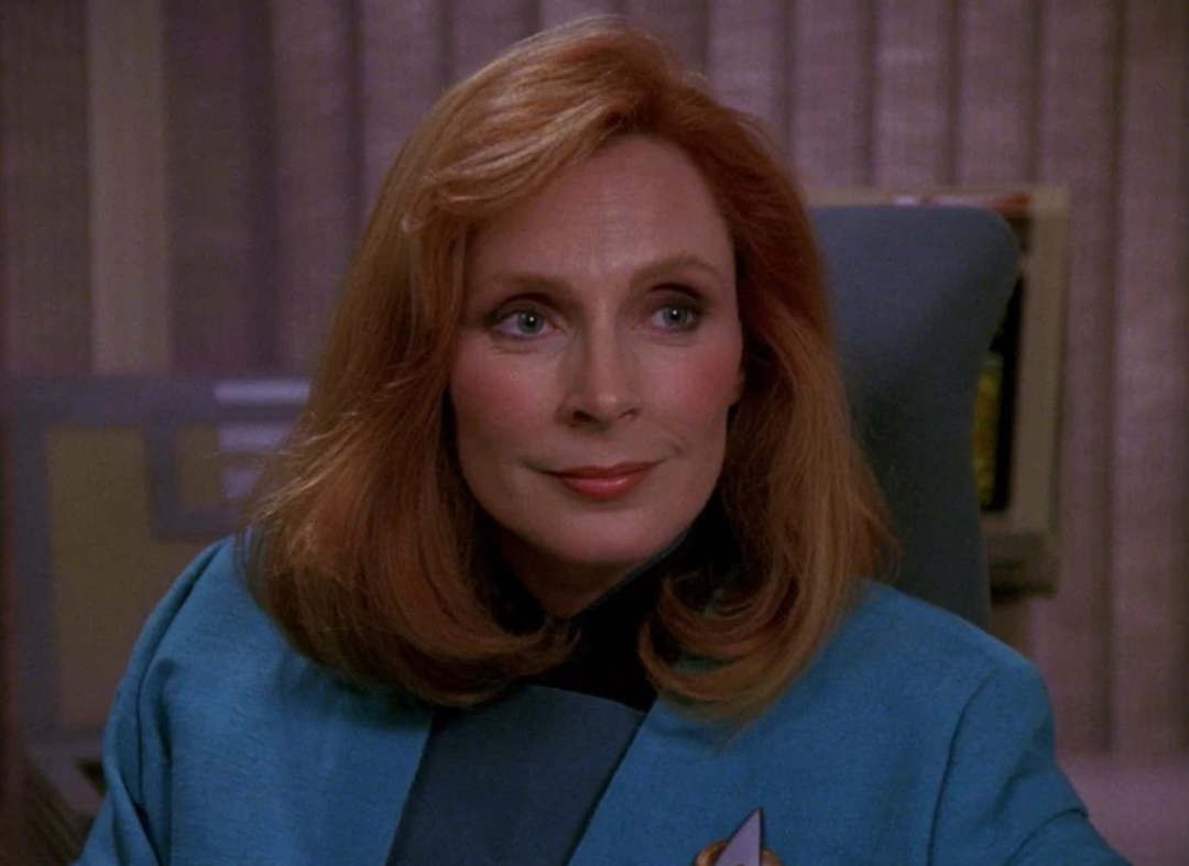 Gates McFadden as Beverly Crusher in a blue Star Trek Uniform.