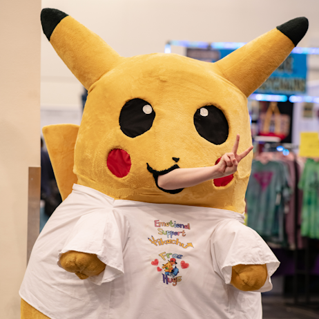 Cosplayer in a pikachu suit with a hand sticking out its mouth with a peace sign
