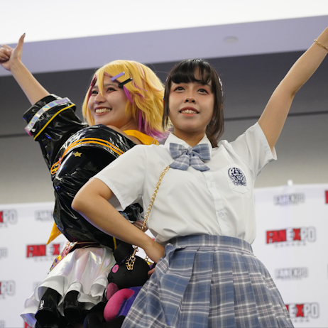 Idolfest Idols smile, with their arms up, giving thumbs up. They are posted back to back in front of a white FAN EXPO Canada background.