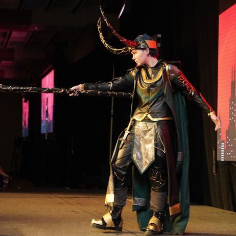 On the main stage, a Loki cosplayer extends their staff toward the audience. Their horns are long, and they have a flowing green cape. 