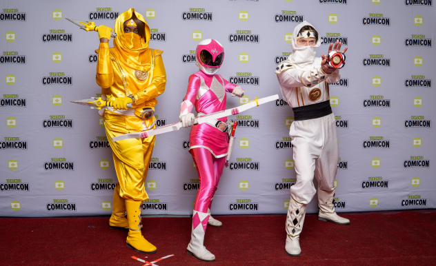 The yellow, pink, and white power rangers take the carpet holding their signature weapons.