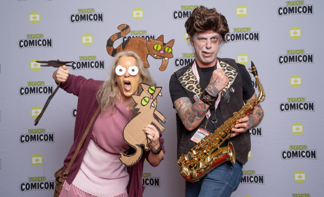 Cosplayers dressed as the Simpsons characters (Elenor Abernathy) and a young Homer, pose with props. She has her selection of cats, and he holds a saxophone.