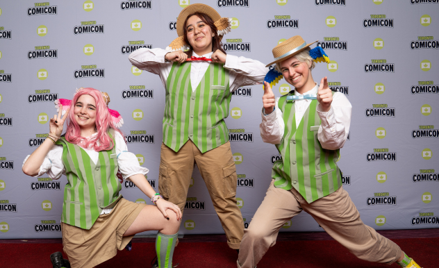 Three cosplayers wearing khaki shorts and green striped vests wear hats and bird wings in their wigs.