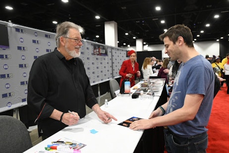 Jonathan Frakes signs a headshot for an excited fan at his table in the celebrity autograph area
