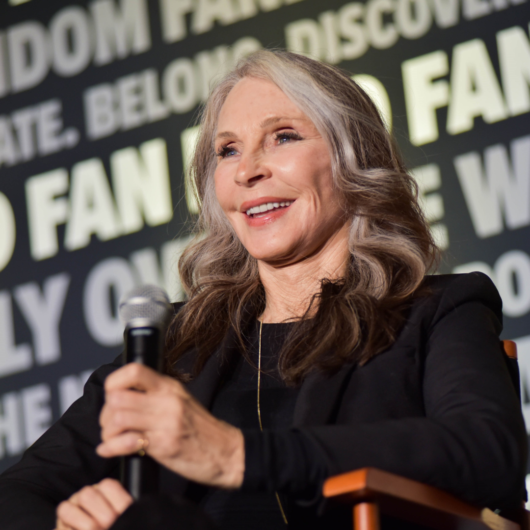 Gates McFadden wearing a black suit sitting on a FAN EXPO panel.