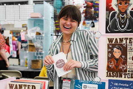 A vendor smiles while holding their art