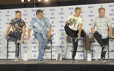 Elijah Wood, Sean Astin, Dominic Monaghan, and Billy Boyd on stage, with their right leg crossing over their left, learning to do a line dance
