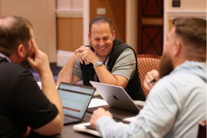 IT professionals gathered around a roundtable discussion with laptops, collaborating, sharing ideas, and discussing practical solutions to service and support challenges.