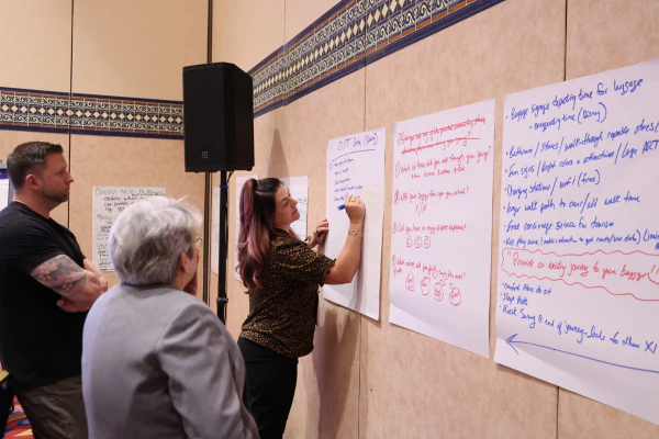 Workshop participant adding notes to a Post-it board as other attendees collaborate nearby.