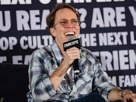 James Arnold Taylor smiling and laughing, holding a microphone.