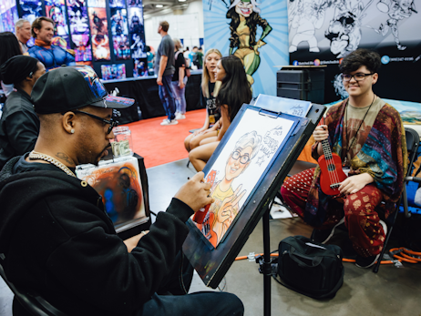 A man drawing a Caricature piece for a young boy sitting in a chair, holding a red guitar.