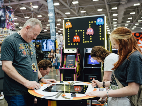 a man (left) and a woman (right) smiling and playing an arcade game built into a table.