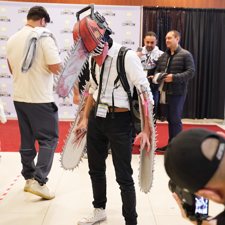 A Denji cosplayer, with chainsaw heard and arms, poses as a photographer shoots their photo on the show floor