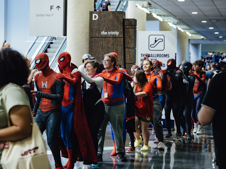 A group of Spider-Man cosplayers in a conga line, dancing through the show lobby.