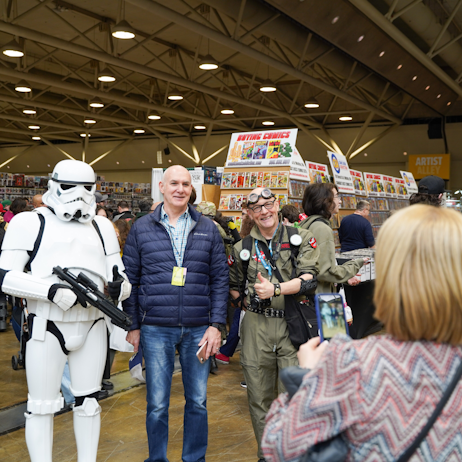 A man poses between a storm trooper and a ghostbuster as his with takes a photo.