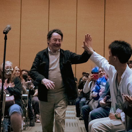 Peter Cullen high fiving a fan in the audience as he walks to his panel