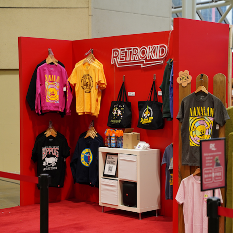 The large, red Retrokid booth, ready for fans to approach and shop. Has shirts and sweaters from franchises like Nanalan, Telefrancais, The Big Comfy Couch and Reading Rainbow.
