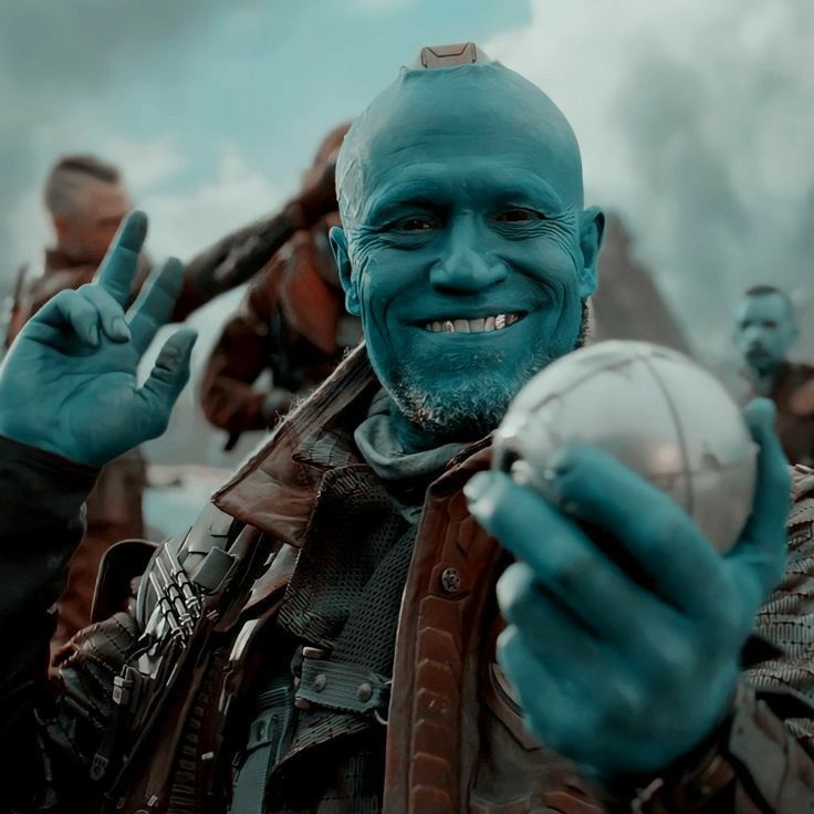 Yondu is smiling directly at the camera and is holding up a metal ball. He looks very happy.