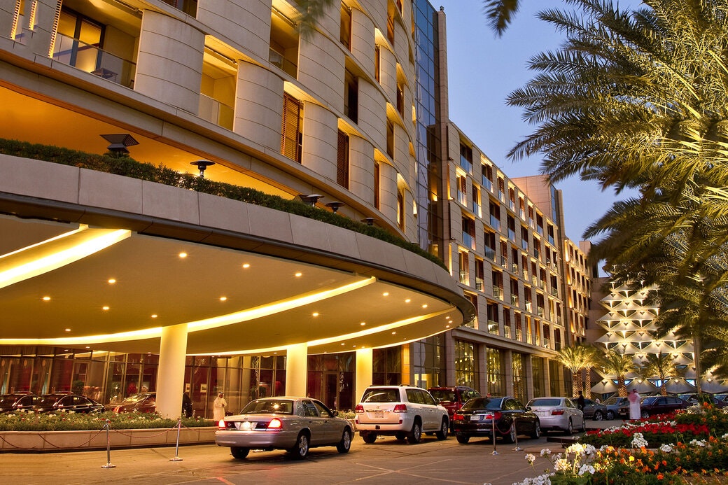 Hotel entrance at dusk with illuminated canopy and lined palm trees