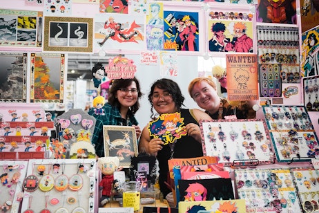 3 vendors pose together smiling while holding their art