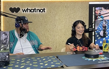 moderator and Ming-Na Wen setting at a table, talking into microphones, doing live signatures at Whatnot booth