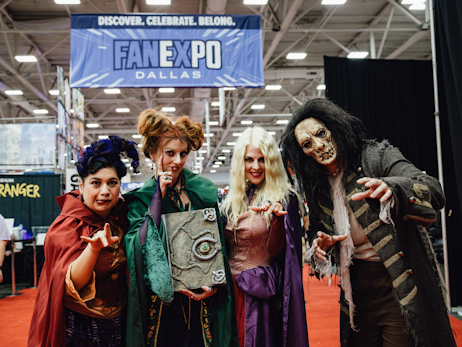 A group of cosplayers dressed as the Sanderson sisters and Billy from Disney's Hocus Pocus, with a FAN EXPO Dallas banner in the background.
