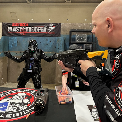 One of the members of the 501st Garrison demonstrates for us how Blast - a - trooper works, pointing the blaster at the trooper in a sleek black suit.