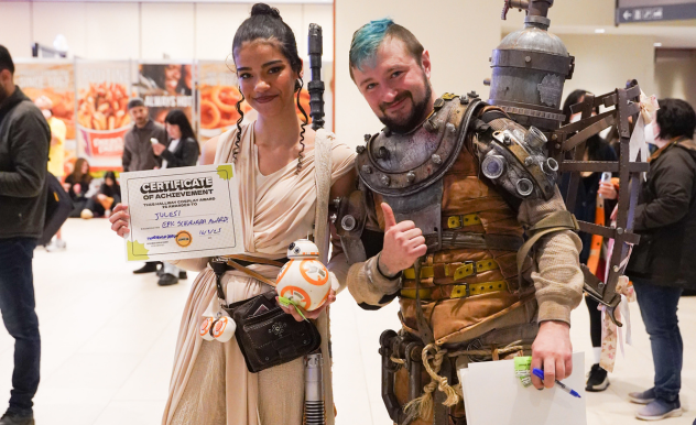 Unorthodox Design poses with a Rey (Star Wars) cosplayer and their award. He gives a thumbs up, they hold a BB8