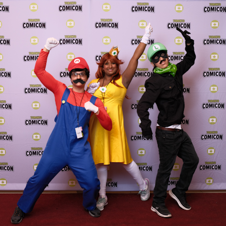Fans posing on the Cosplay Red Carpet in front of the Toronto Comicon backdrop. Left to right: Mario, Princess Daisy, Luigi.