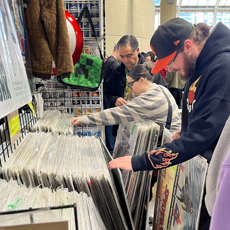 Two fans flip through large movie posters at one of our vendors. One wearing a striped white and blue sweater. The other in a black hoodie embellished with flames