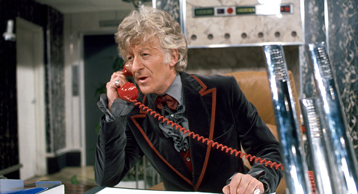 On the TARDIS, Sat behind a desk, the Doctor answers a red telephone
