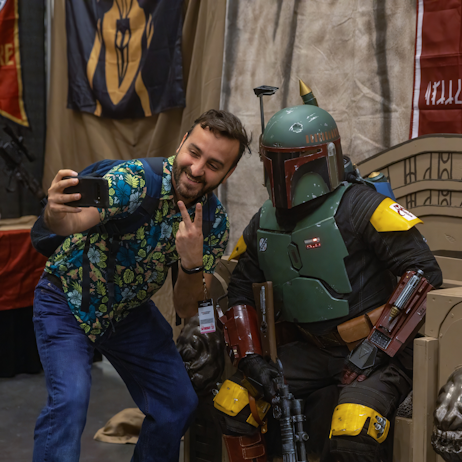 A Fan taking a selfie of a cosplayer as Boba Fett on his throne