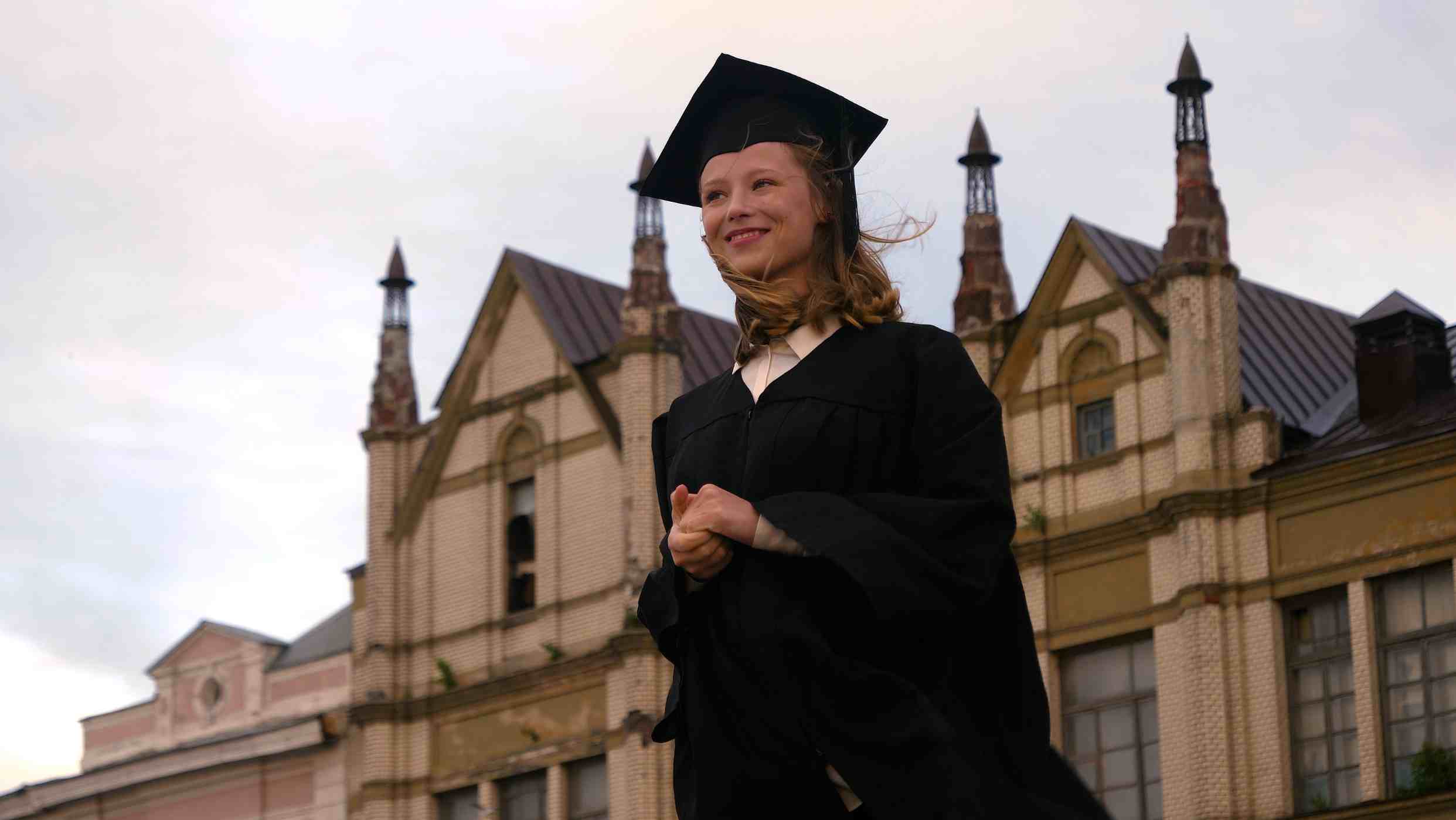 Student wearing graduation gown in front of university