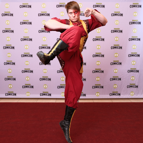 A cosplayer dressed as Zuko from Avatar: The Last Airbender leaps in a kicking motion toward the camera. His suit is red with yellow details and he has a port wine birth mark over his eye
