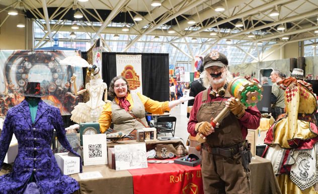 Toronto Steampunk Society members pose with their booth. Featuring costumes, props, and art. The member in the foreground is steam punk Mario.