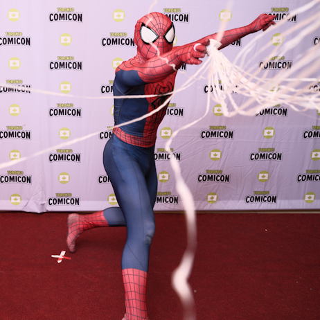 Spider-Man, on the cosplay red carpet, faces the camer and slings strands of long rope web.