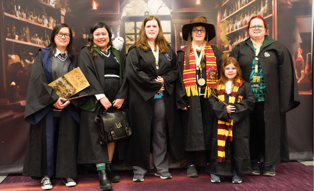 Fans of all ages pose in front of a Hogwarts backdrop for a Harry Potter Cosplay meetup.