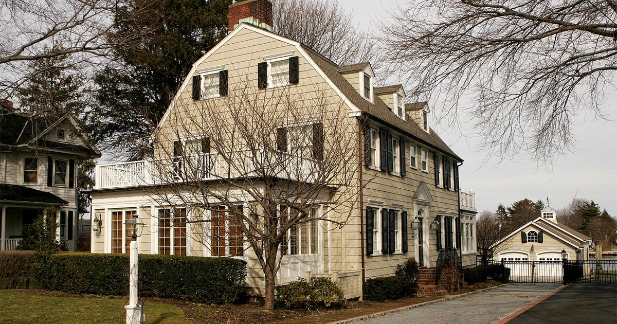 An angled shot of the house from the street on the left hand side. The side second floor balcony shows prominently in the foreground with bare trees framing the home. The two door garage looks like a smaller version of the beautiful, 3 floor, beige home.