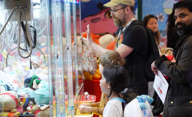 Two dads assist their children who are playing separate claw machine games