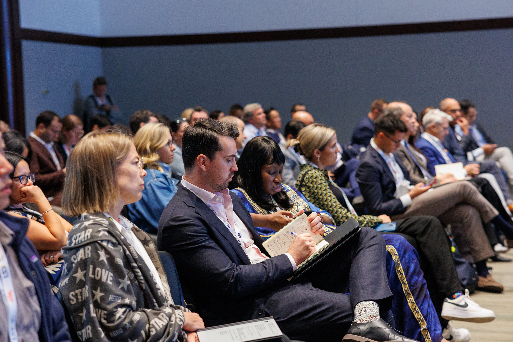 Audience members are seated and take notes during a speaker's session.