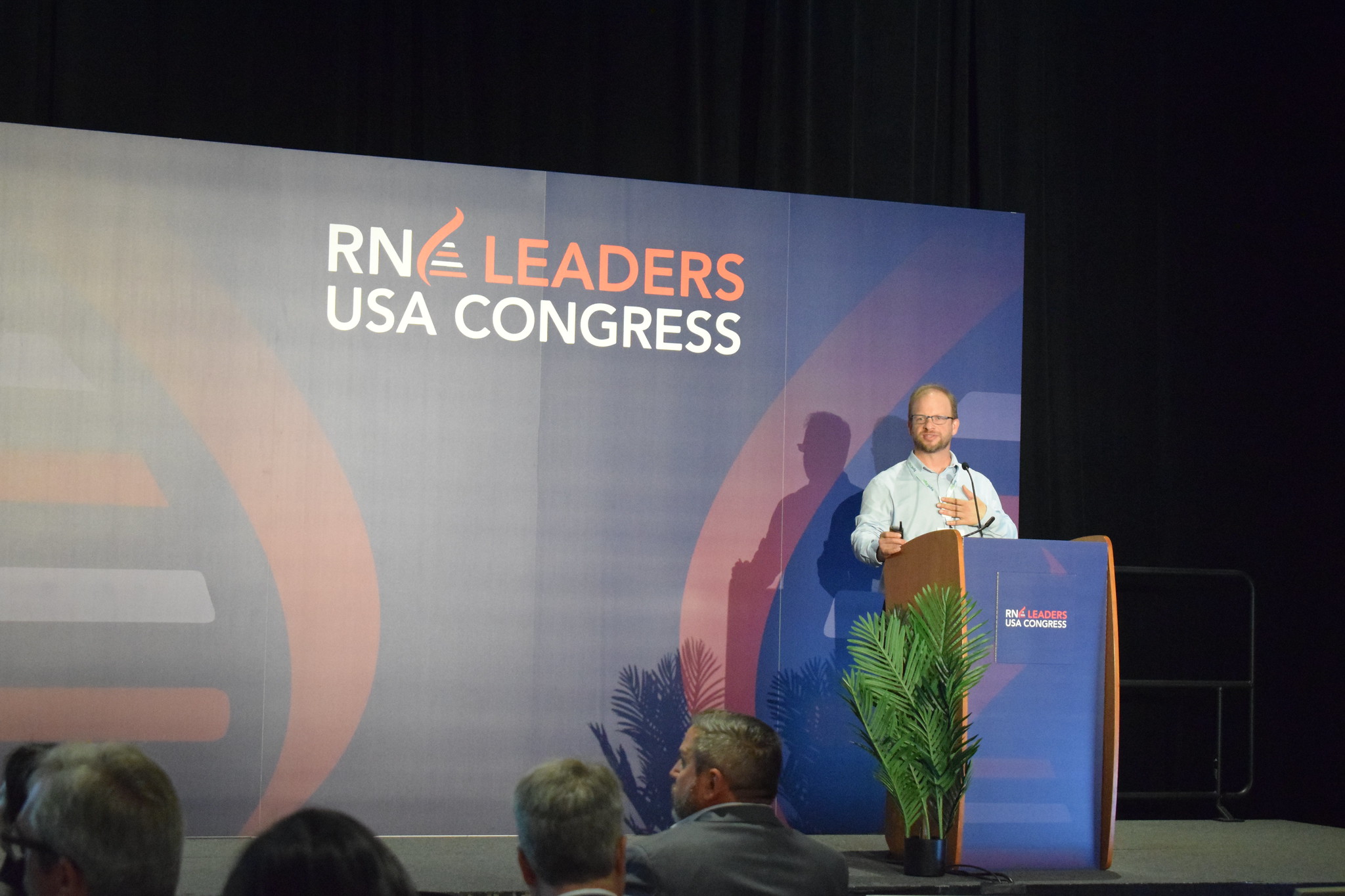 A speaker talks at a podium on stage with the RNA Leaders USA Congress Logo in the background.