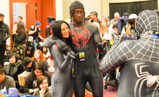 A pair of fans dressed as Spider-Man and Miles Morales pose together for a photo.